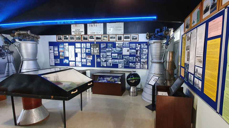 The Blue Streak museum display. There are artefacts displayed on the walls and in glass displays. Rocket engine bells are displayed on either side of the room.